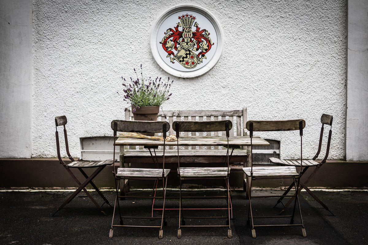 Sitzbereich im Innenhof der Hoffer Alter Brennerei mit Holzstühlen, Tisch und dekorativem Wappen an einer weißen Wand.